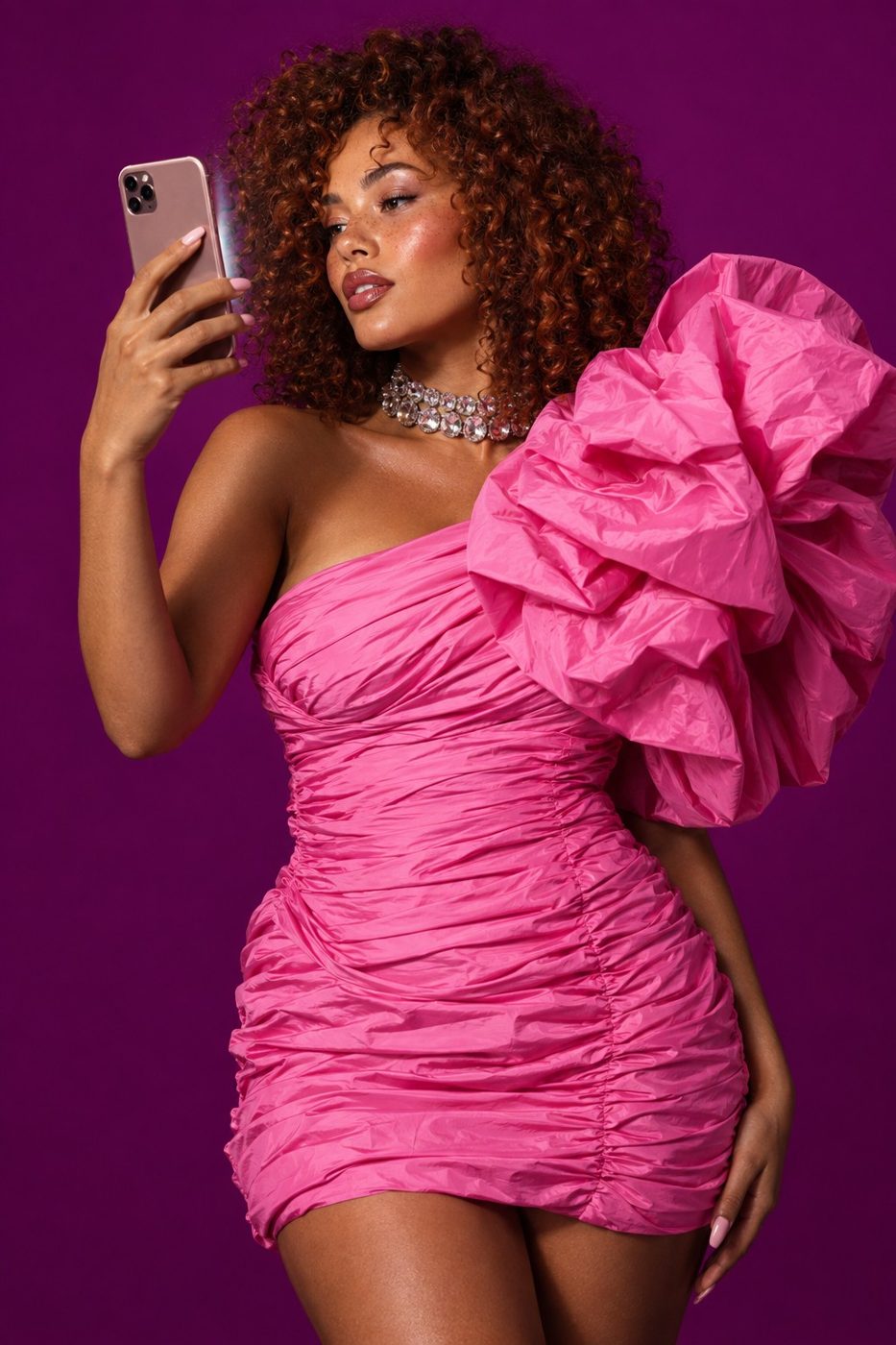 Creadora con vestido rosa plisado mirándose en el móvil sobre fondo violeta